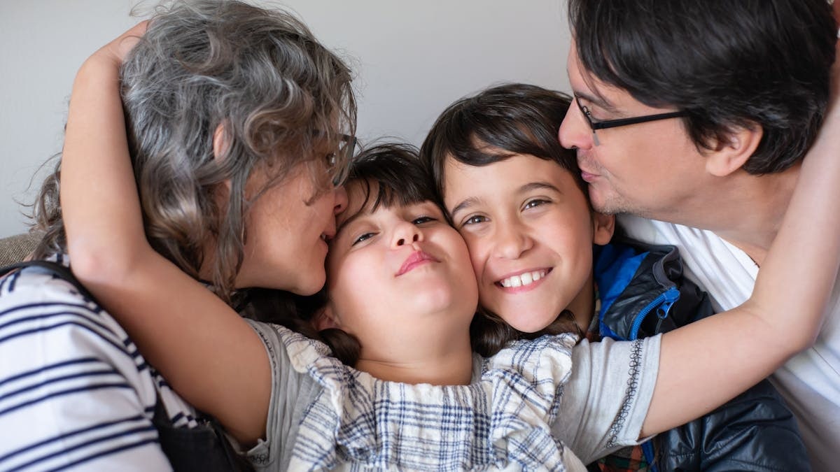 A joyful family of four sharing a warm embrace, highlighting love and togetherness indoors.